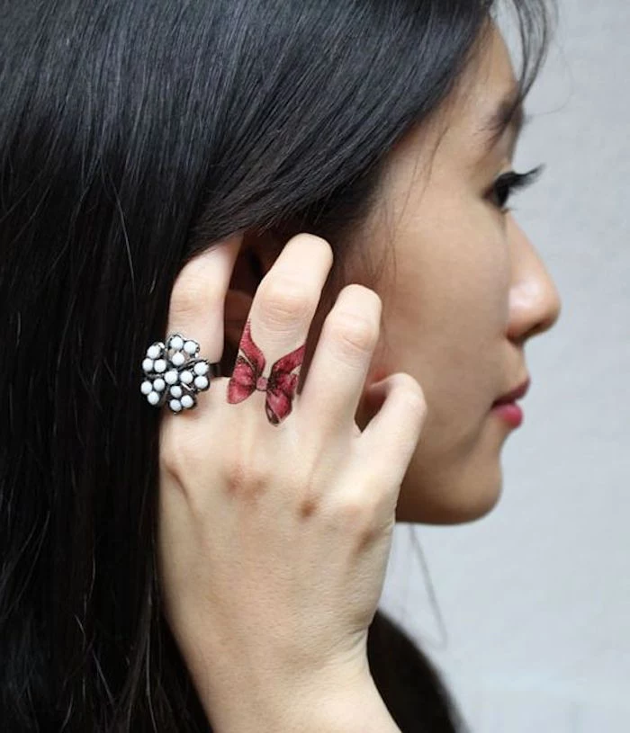 woman holding her black hair, white pearl ring, red bow, middle finger tattoo, finger tattoos for women