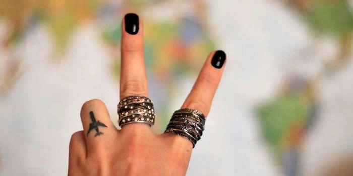 hand making a peace sign, small airplane, ring finger tattoo, finger tattoos for women, black nail polish