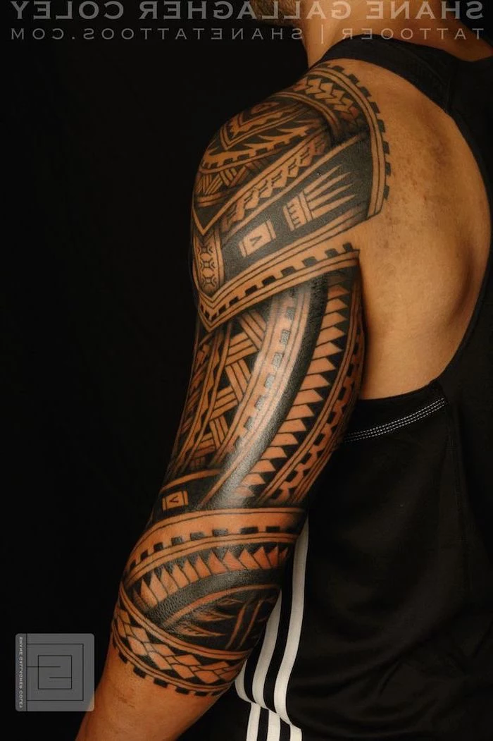 cool small tattoos, large tribal, arm sleeve tattoo, man wearing a black top, standing in front of a black background