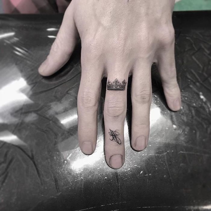small crown and the letter a, finger tattoos, cool small tattoos, hand resting on a table, covered in nylon