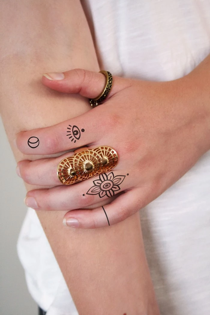 large golden ring. flower eye and moon finger tattoos, heart tattoo on finger, white shirt
