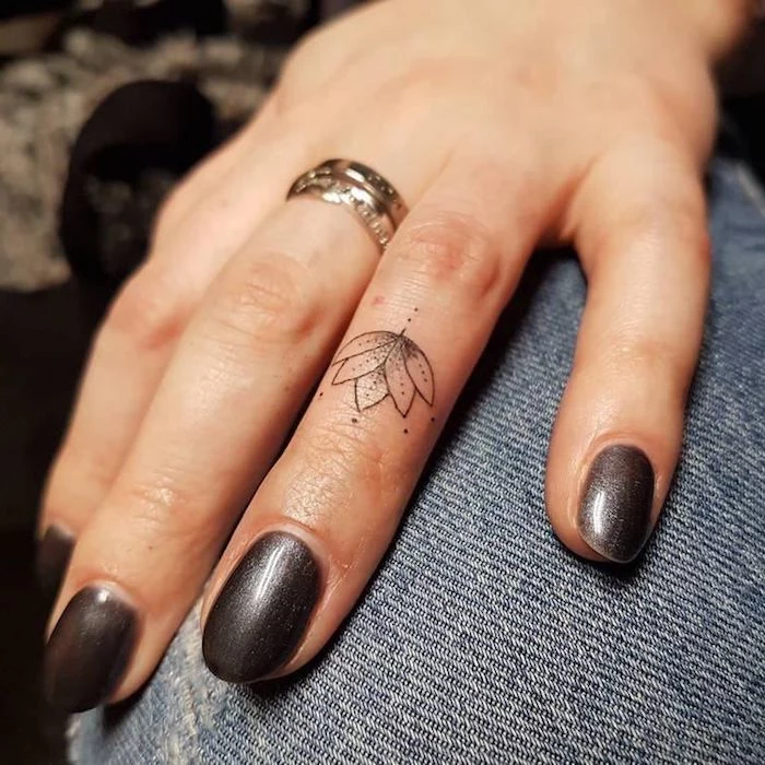 lotus flower, ring finger tattoo, heart tattoo on finger, grey nail polish, hand resting on jeans