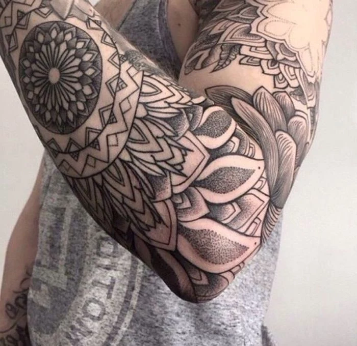 large black and white, arm sleeve tattoo, man wearing a grey top, cool small tattoos, white background