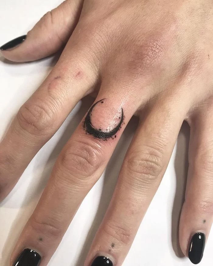 crescent moon tattoo, on the middle finger, finger tattoos, hand resting on a white countertop