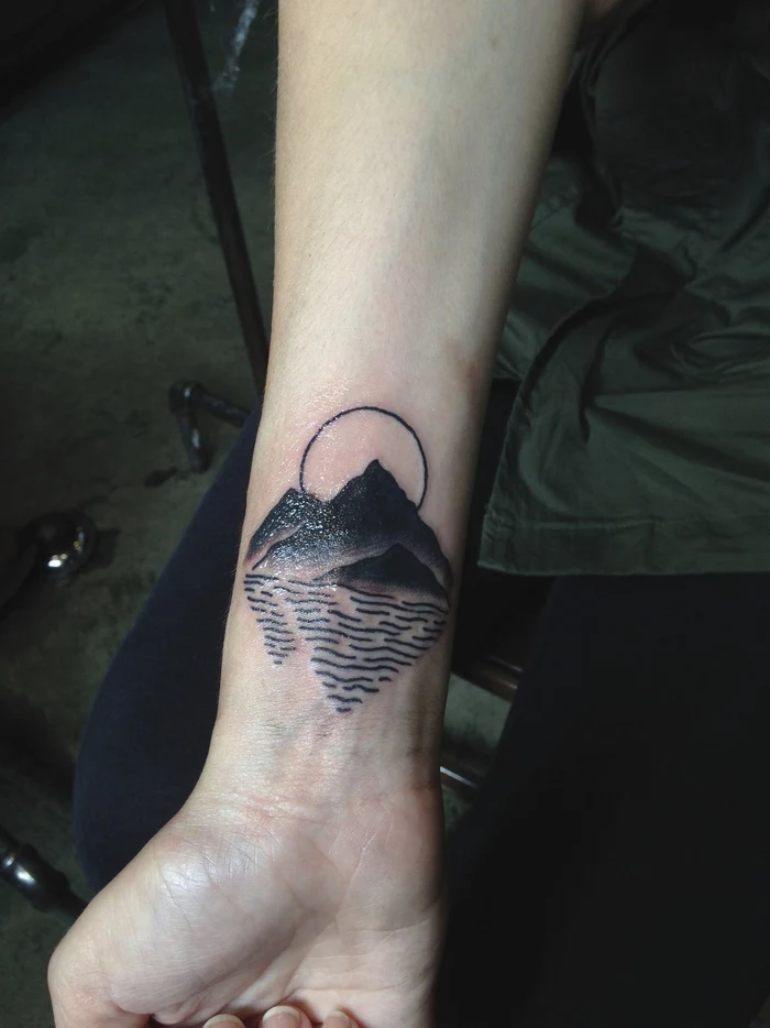 mountain landscape with river, geometric flower tattoo, tattoo on the wrist of a girl