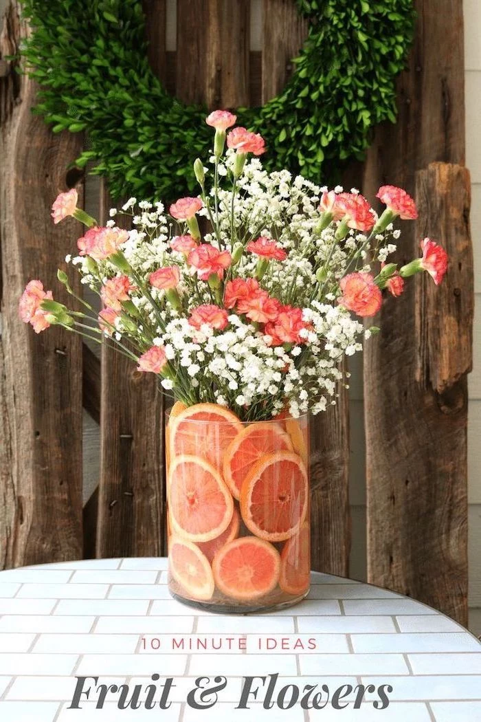 large round vase, filled with orange slices, flower arrangement ideas, orange carnation flowers and baby's breath