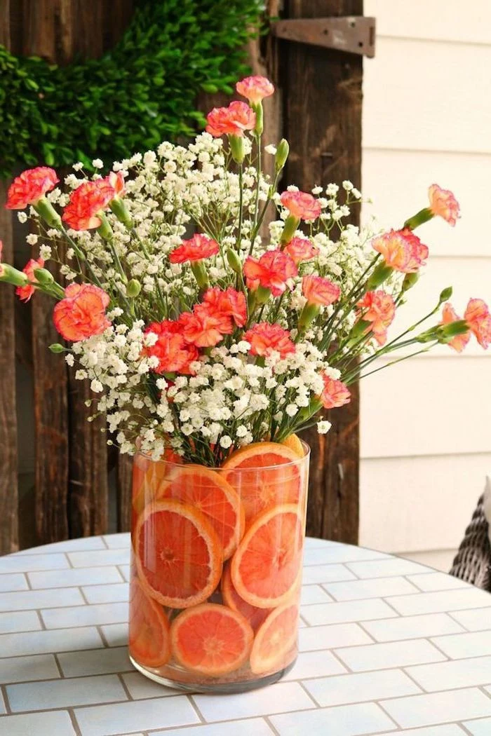 large round glass vase, filled with orange slices, orange carnation flowers, and baby's breath, floral arrangements