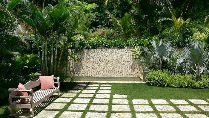 cement tiles, over a patch of grass, small wooden bench with pink throw pillows, small backyard designs, planted palm trees