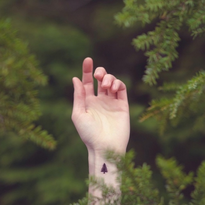 pine tree wrist tattoo, small butterfly tattoos, hand amongst pine trees in a forest
