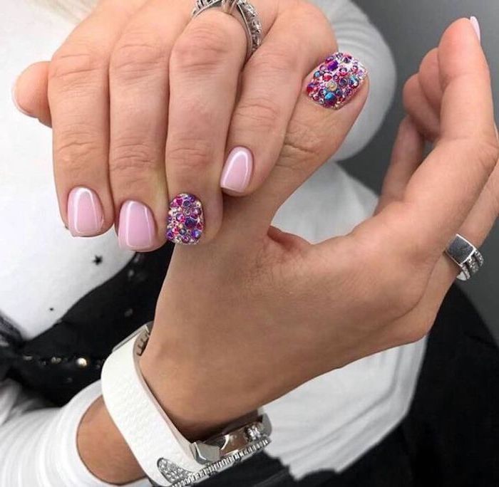 pink nail polish, colourful rhinestones on two nails, white watch on the wrist, nude matte nails