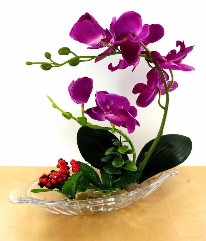 purple orchid, in a very small glass plate, with river stones, beautiful flower arrangements, on a wooden table