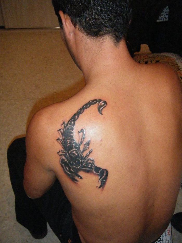 3d scorpion, shoulder tattoo, man sitting down, inner arm tattoos, man wearing black trousers