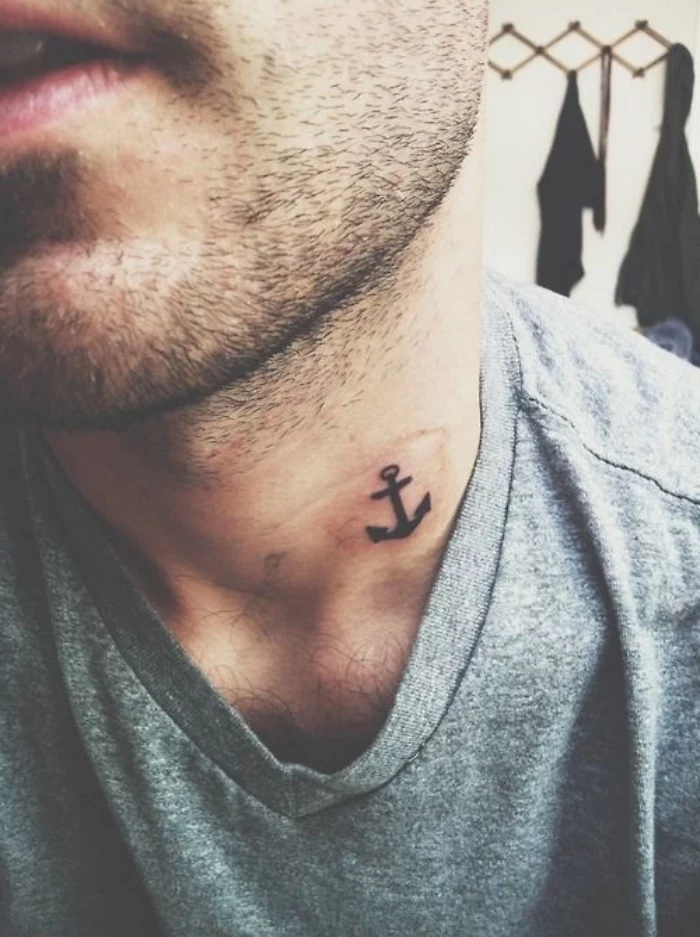 small anchor neck tattoo, man with a black beard, wearing a grey shirt, small sunflower tattoo