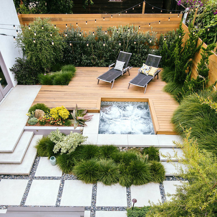 cement tiles, leading to a small hot tub, two lounge chairs, small backyard ideas, planted trees and bushes