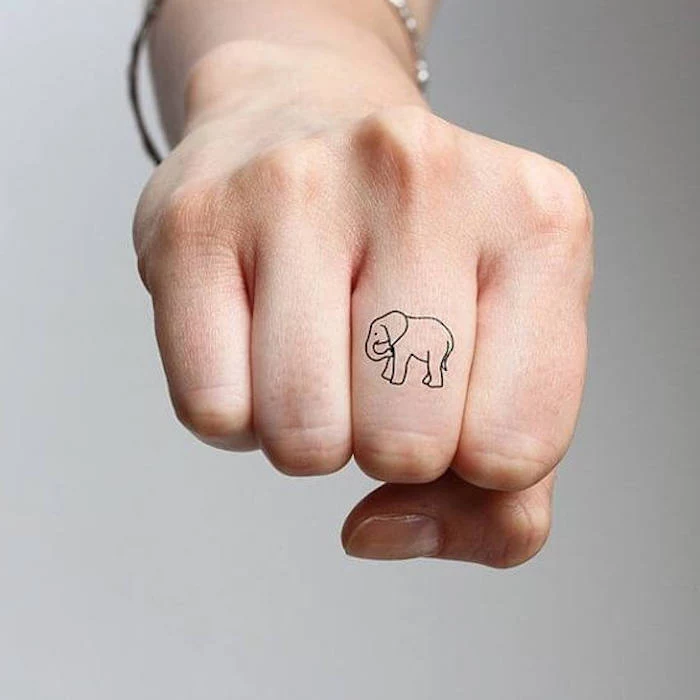 small elephant, middle finger tattoo, couple finger tattoos, hand in a fist, in front of a grey background
