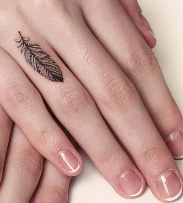 small feather, ring finger tattoo, couple finger tattoos, hands on top of one another, in front of a white background