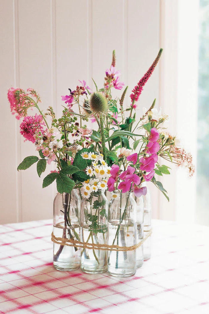 glass bottles arranged in a one centerpiece, different colourful flowers, diy flower arrangements