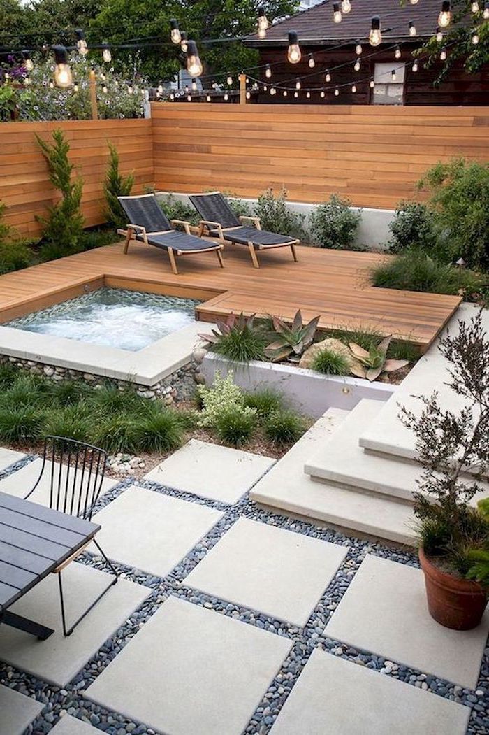 small hot tub, surrounded by wooden floor, with two black lounge chairs, small backyard landscaping