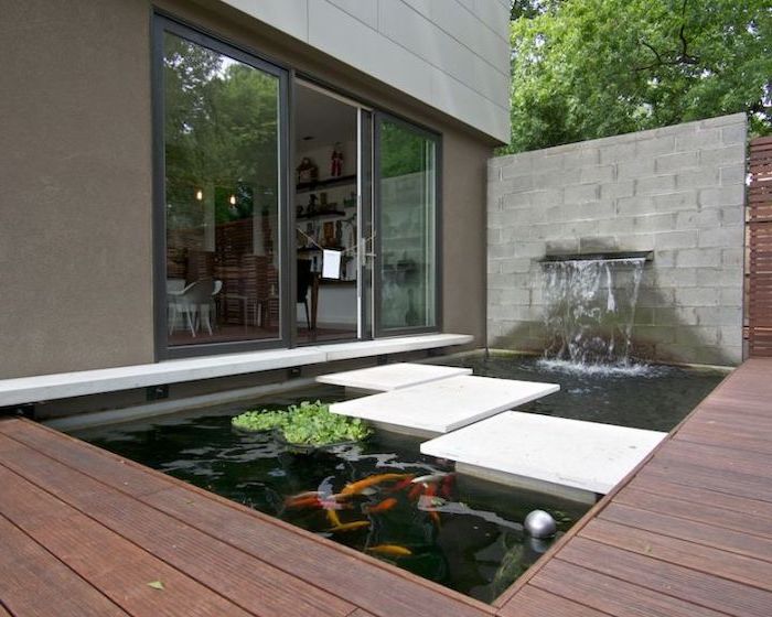 small pond, with a water fountain, cement tiles over the pond, small backyard landscaping, tall windows