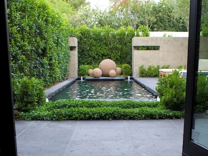 small pool, with small fountains, large round rocks, small backyard landscaping, surrounded by tall hedges