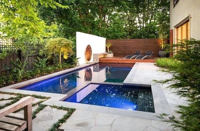 small swimming pool, with a small hot tub, small yard landscaping, two black lounge chairs