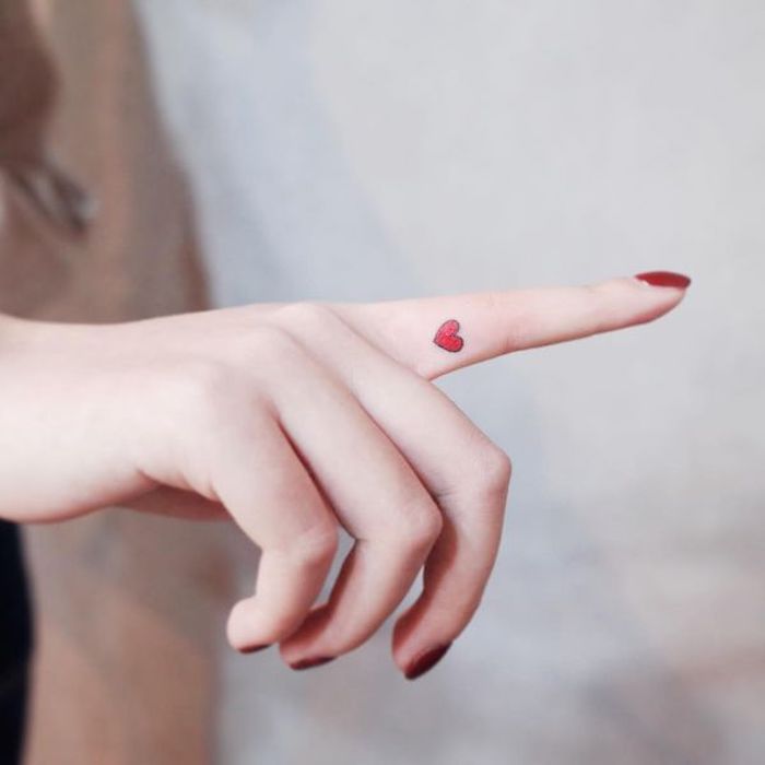 small red heart tattoo, red nail polish, crown finger tattoo, hand in front of a white background