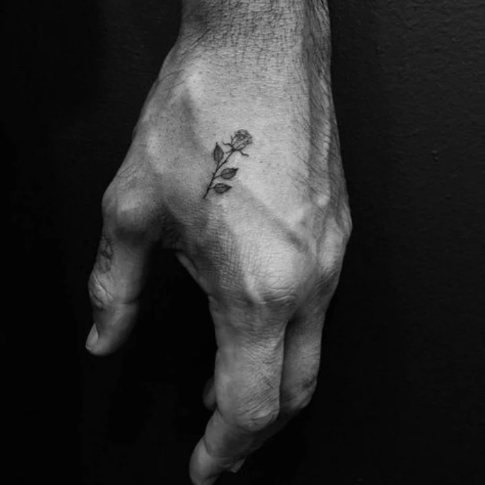rose hand tattoo, men's hand in front of a black background, cool small tattoos for guys