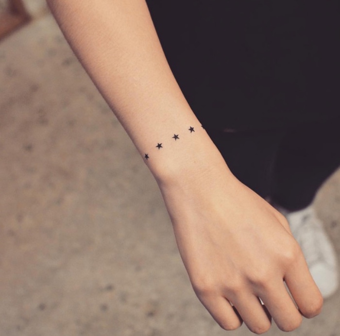 small black stars tattoo around the wrist, small forearm tattoo, person wearing all black