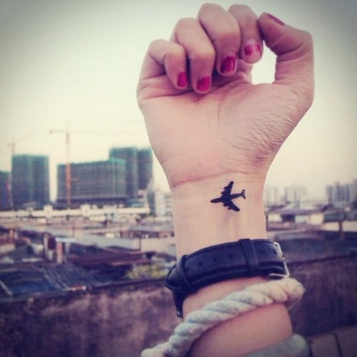 small black airplane wrist tattoo, small forearm tattoo, city landscape in the background