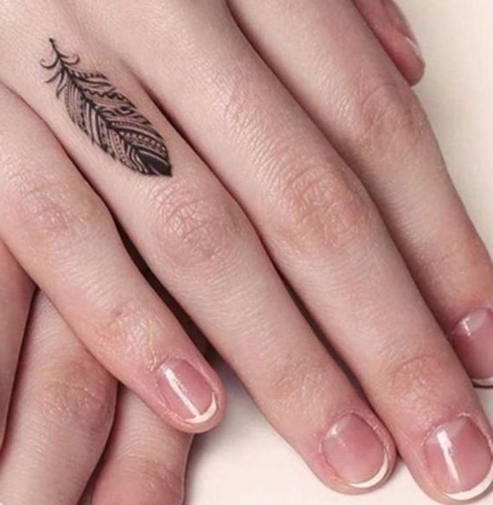 small black feather finger tattoo, small forearm tattoo, woman with a french manicure
