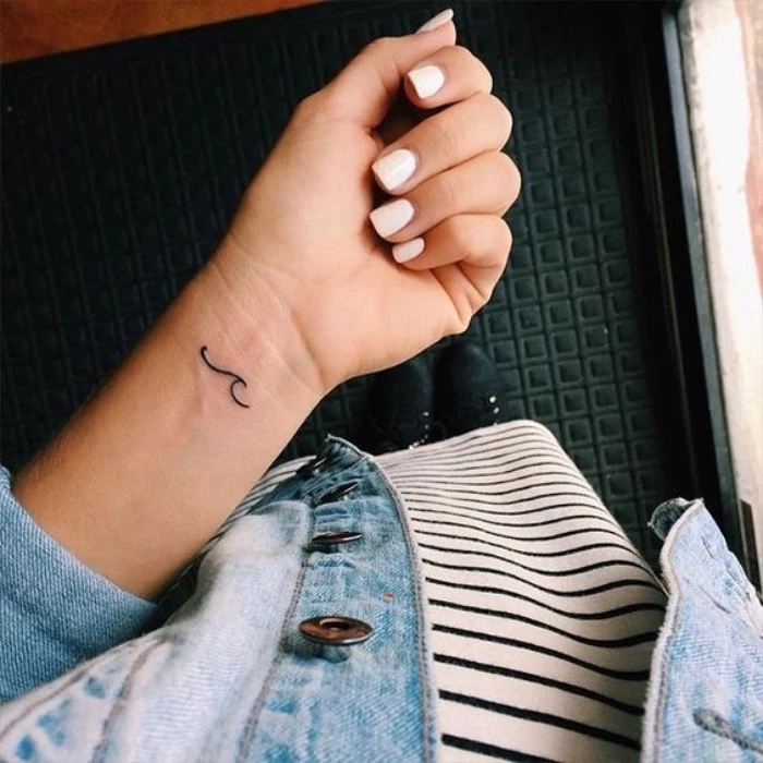 small lotus flower tattoo, small wave wrist tattoo, woman with white nail polish, wearing a jean jacket