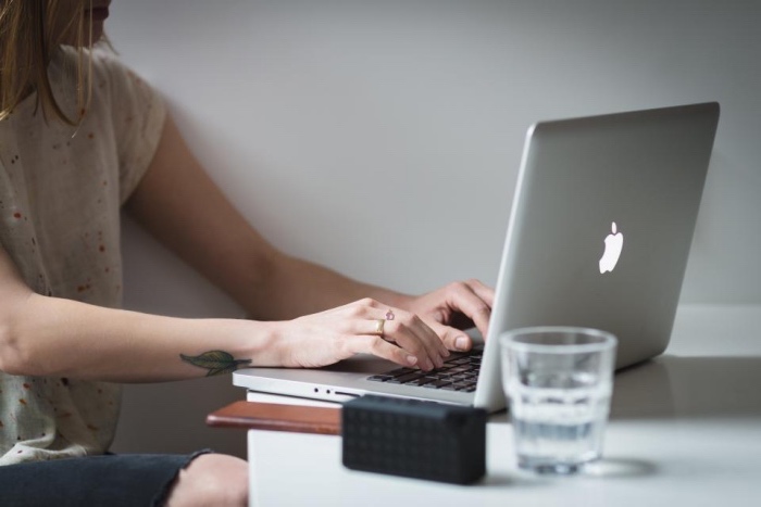 woman sitting down, typing on a macbook, leaves wrist tattoo, small lotus flower tattoo