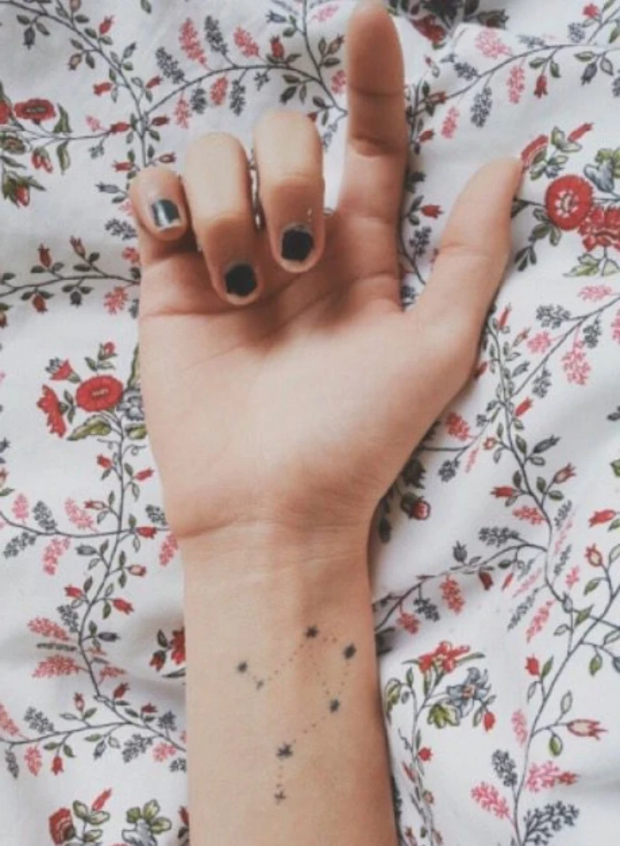 hand laying on floral bed linen, small lotus flower tattoo, star constellation wrist tattoo