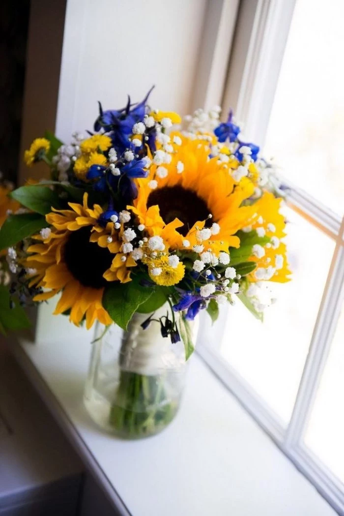 sunflowers and blue flowers, small flower bouquet, in a glass round vase, in front of a window, flower arrangement pictures