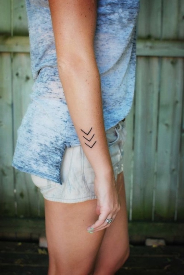 arrows pointing down forearm tattoo, small tattoo ideas for women, wearing a blue top and shorts