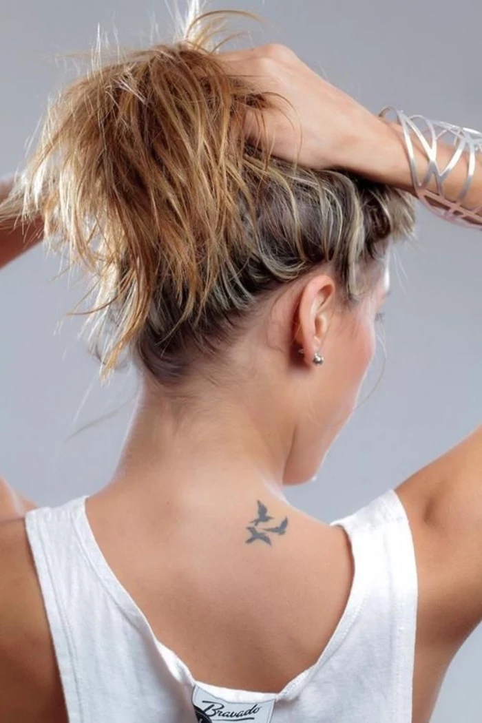 three birds flying back tattoo, woman tying her hair in a ponytail, small tattoo ideas for women, wearing a white top