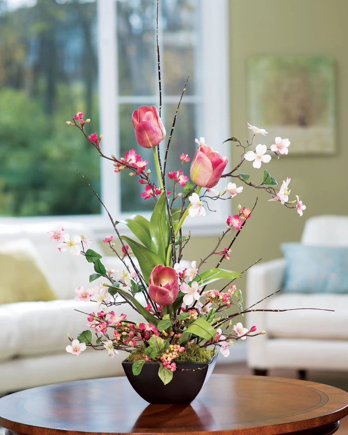 silk flower arrangements, pink tulips, small magnolias, in a small pot with moss, on a round wooden table