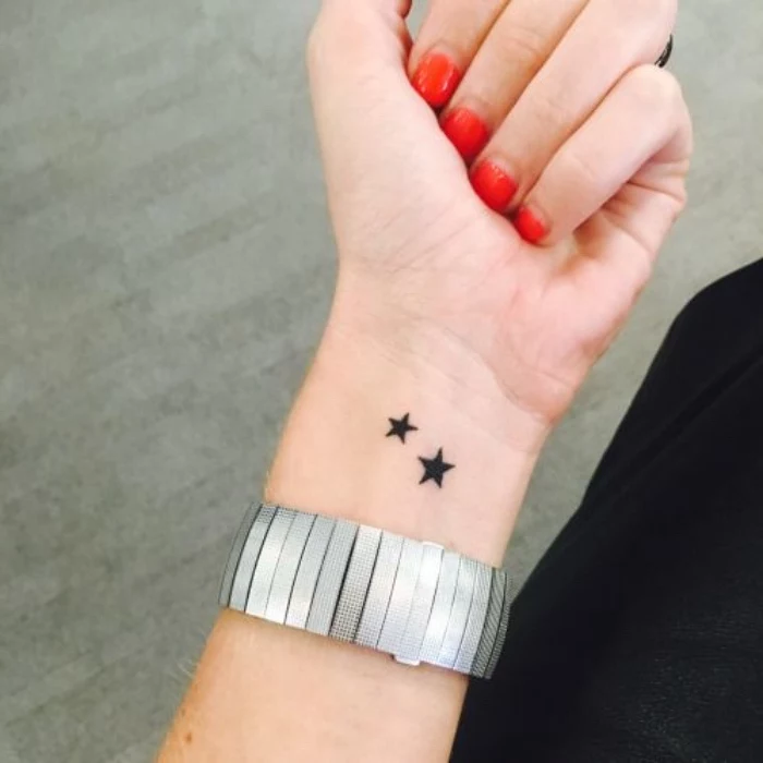 best small tattoos for men, two black stars wrist tattoo, large silver bracelet, red nail polish