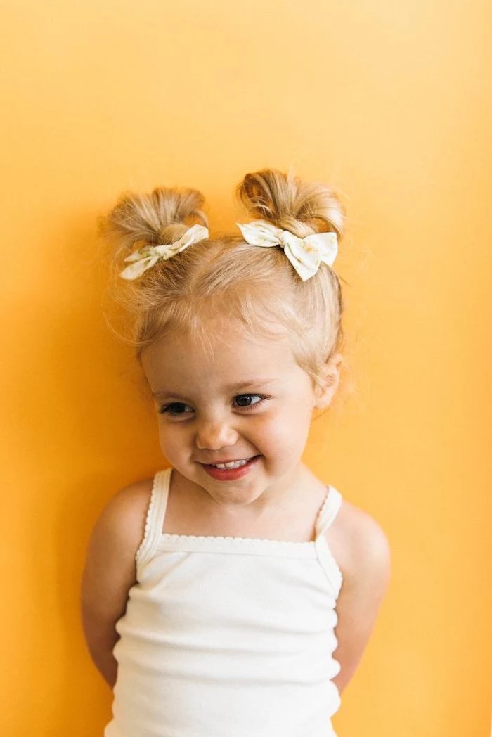 yellow background, kids braided hairstyles with beads, two floral bows, blonde hair in two messy buns