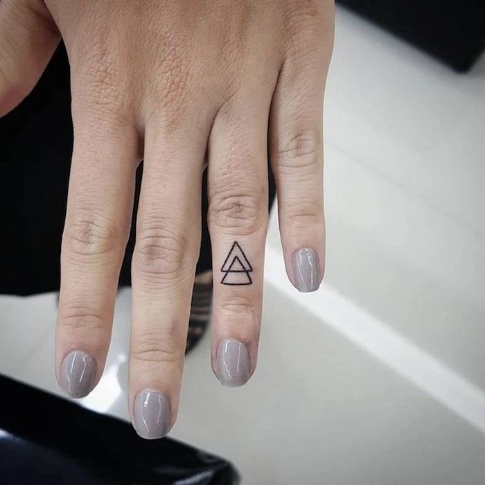 two intertwined triangles, on the ring finger, finger tattoo, hand with grey nail polish