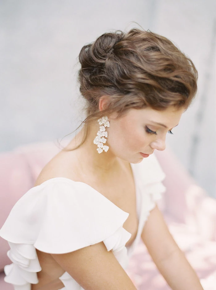 brown wavy hair, in a low updo, long earrings, wedding hairstyles for medium hair, white dress