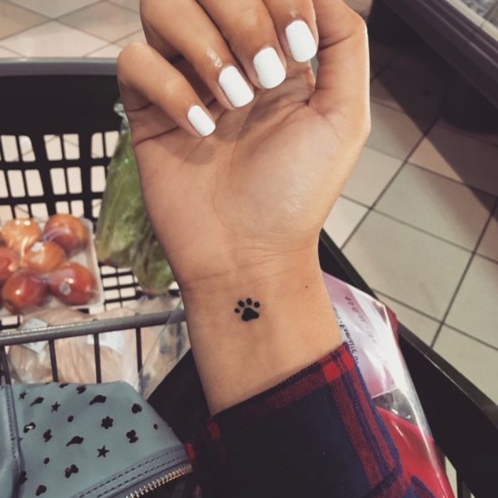 white nail polish, shopping cart in the background, best small tattoos for men, small black dog pow wrist tattoo