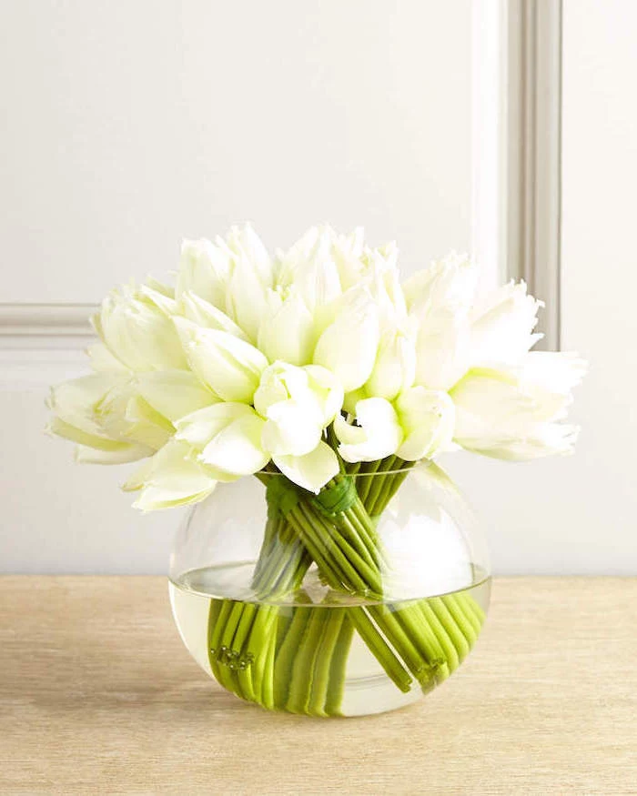 white tulips, in a glass round vase, mason jar flower arrangements, on a wooden table, in front of a white wall