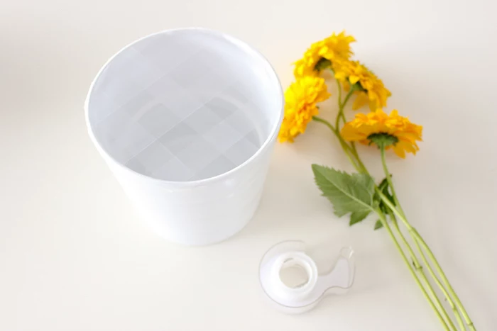 yellow flowers and tape, on a white countertop, flower centerpieces, white vase with tape on it