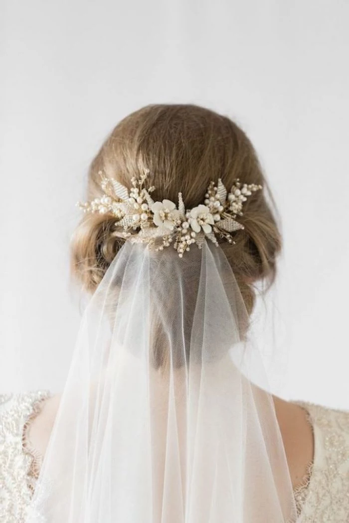 white veil, with a floral hair clip, blonde hair in a low updo, bridesmaid hairstyles, white background