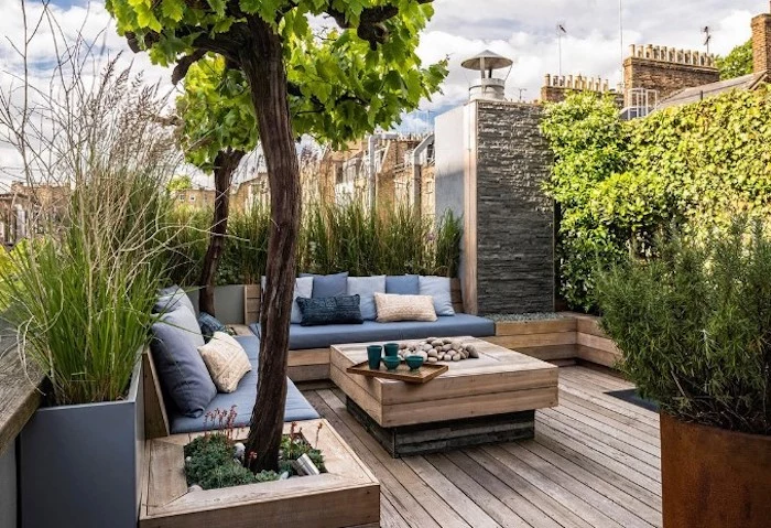 wooden garden furniture, with colourful throw pillows, planted trees and bushes, small patio ideas