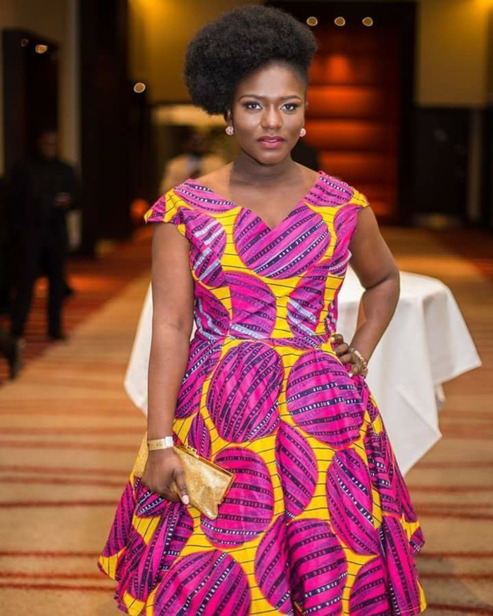 mid length dress, african attire, black hair, in a high updo, golden clutch, table in the background