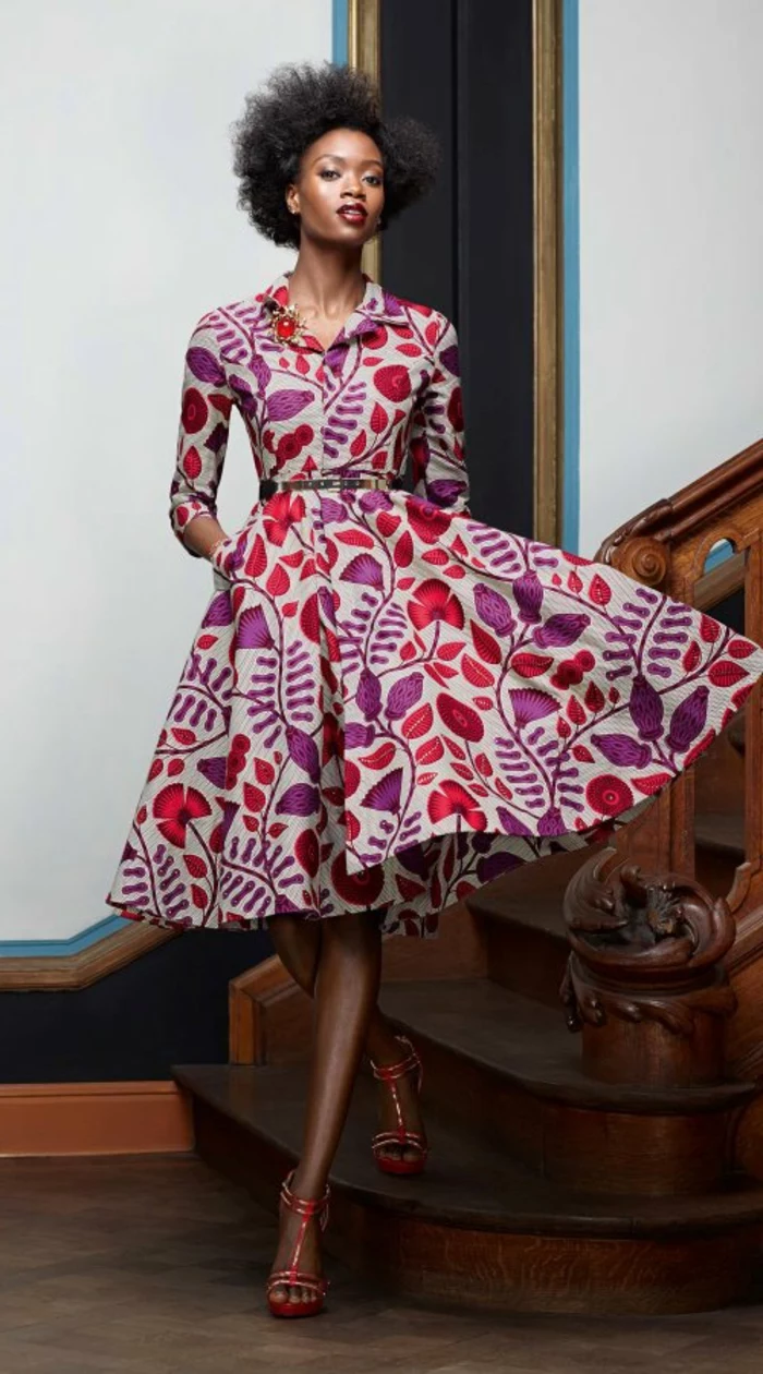 woman standing on a wooden staircase, wearing a mid length dress, red high heel sandals, african print