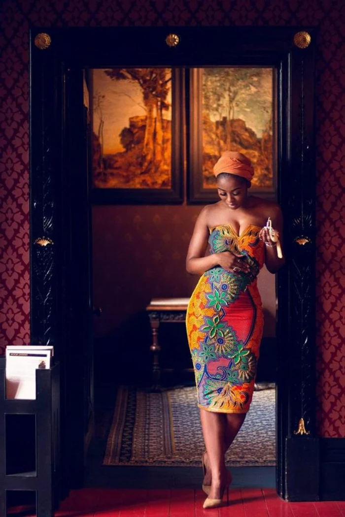 woman standing in the doorway, wearing a dress, african print, orange headscarf. nude heels