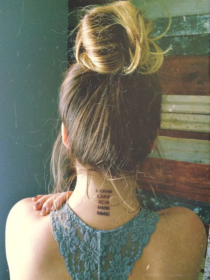 blonde hair in a messy bun, blue lace top, back tattoo, roman numerals, blue backgorund